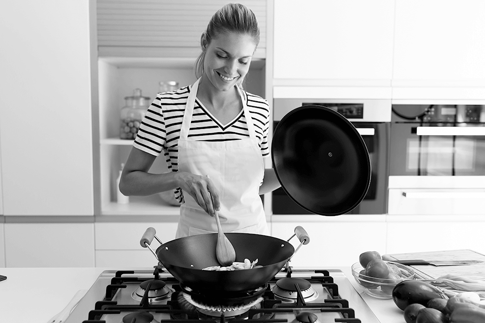 Shot of healthy young woman cooking and mixing food in frying pan in the kitchen at home.